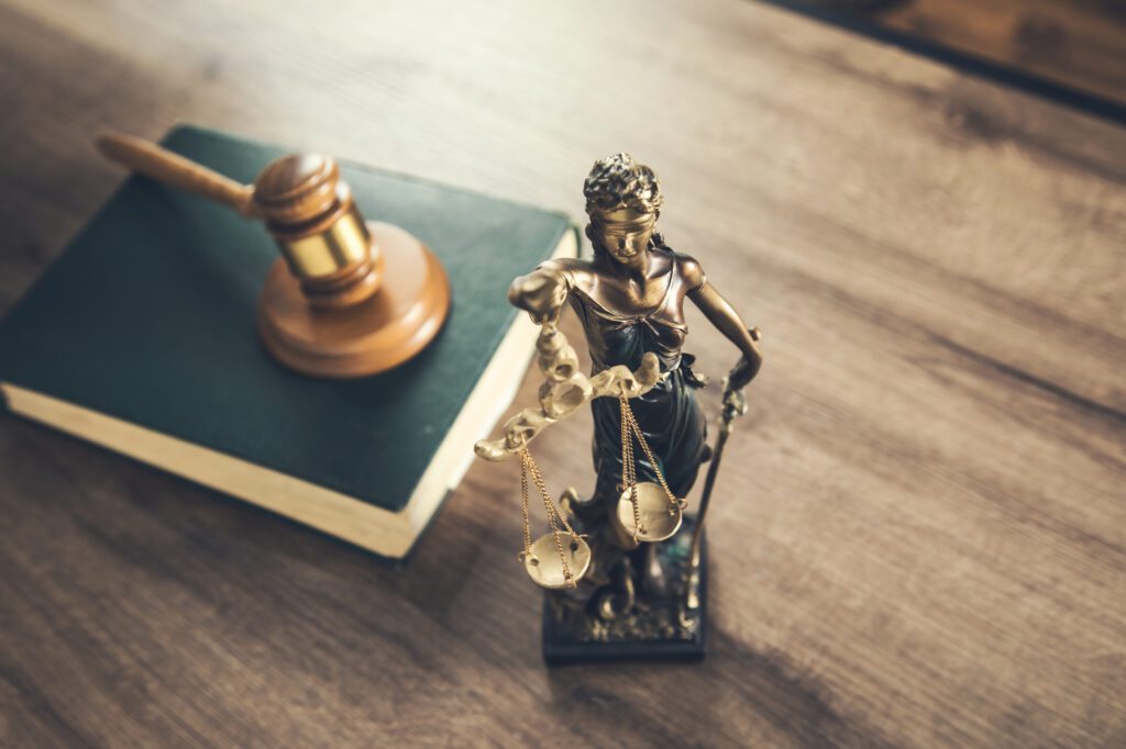 Lady Justice statue with gavel and law book on wooden desk symbolizing legal justice
